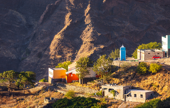 Aerial view of colorful village buildings nestled against the rugged volcanic mountain slopes of Santo Antao during golden hour in Alto Mira Porto Novo Cabo Verde.