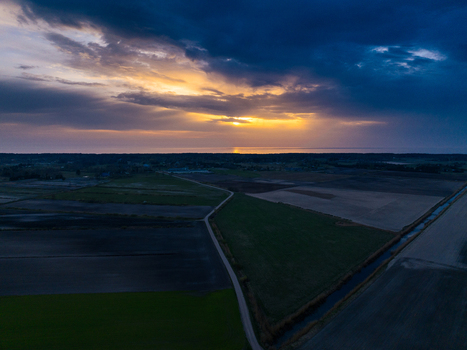 Aerial view of agricultural fields and a narrow road at sunset with a dramatic cloudy sky over the horizon Skatre South Kurzeme Municip Latvia. Aerial view of agricultural fields and a narrow road at sunset with a dramatic cloudy sky over the horizon Skatre South Kurzeme Municip Latvia.