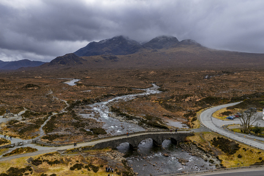 Aerial view of Sligachan Old Bridge crossing a rocky river with the Cuillin mountains under a moody sky in Sligachan Scotland United Kingdom. Aerial view of Sligachan Old Bridge crossing a rocky river with the Cuillin mountains under a moody sky in Sligachan Scotland United Kingdom.