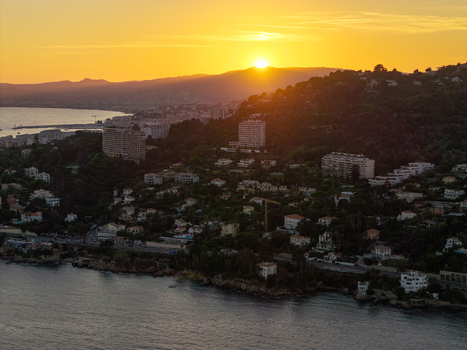 Aerial view of the coastal town at sunset with golden light illuminating the buildings lush hills and the Mediterranean Sea in Antibes Provence Alpes Cote d Azur France. Aerial view of the coastal town at sunset with golden light illuminating the buildings lush hills and the Mediterranean Sea in Antibes Provence Alpes Cote d Azur France.