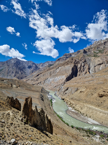 View of the Penzi La road winding through the rugged arid mountain landscape of the Zanskar valley with a glacial river flowing below under a bright blue sky in Zanskar Ladakh India.