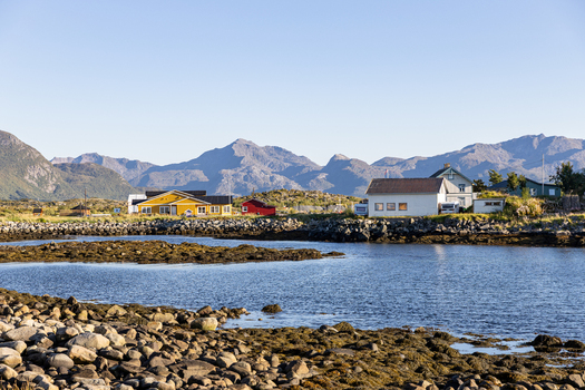 View of colorful houses along a rocky coastline with rugged mountains under a clear sky in Laukvik Nordland Norway. View of colorful houses along a rocky coastline with rugged mountains under a clear sky in Laukvik Nordland Norway.