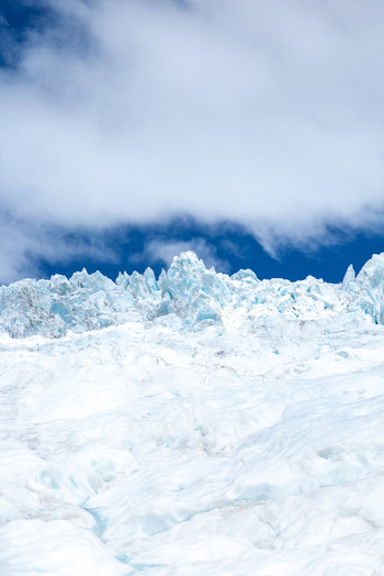 View of a vast expanse of glacial ice stretches under a bright blue sky with scattered white clouds a cold and serene landscape Franz Josef Glacier West Coast Region New Zealand. View of a vast expanse of glacial ice stretches under a bright blue sky with scattered white clouds a cold and serene landscape Franz Josef Glacier West Coast Region New Zealand.