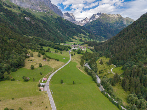 Aerial view of a winding road through the lush green valley of Gadmen surrounded by alpine mountains and dense forests in Gadmen Switzerland.