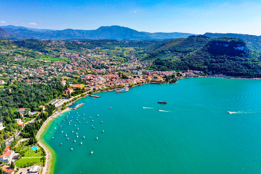 Aerial view of Lake Garda with its turquoise waters anchored boats and the coastal town nestled against lush green hills under a clear blue sky in Italy. Aerial view of Lake Garda with its turquoise waters anchored boats and the coastal town nestled against lush green hills under a clear blue sky in Italy.