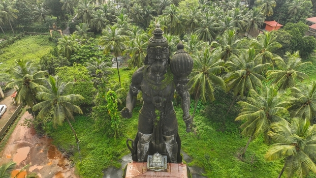 Aerial view of the large stone statue of Lord Hanuman holding a mace surrounded by lush palm trees and dense greenery in Udupi Karnataka India. Aerial view of the large stone statue of Lord Hanuman holding a mace surrounded by lush palm trees and dense greenery in Udupi Karnataka India.