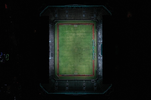 Aerial view of Maguwoharjo Stadium at night with illuminated football pitch and surrounding seating stands in Kecamatan Depok Daerah Istimewa Yogya Indonesia.