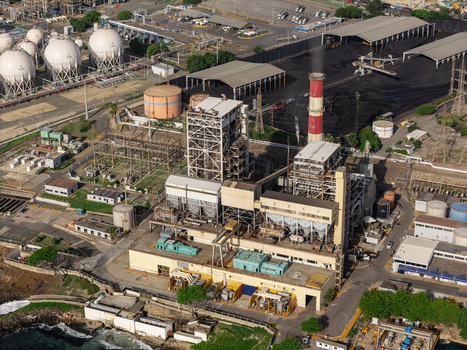 Aerial view of the Haina power plant with storage tanks industrial buildings a tall chimney and coal piles along the coast in Bajos de Haina San Cristobal Province Dominican Republic.