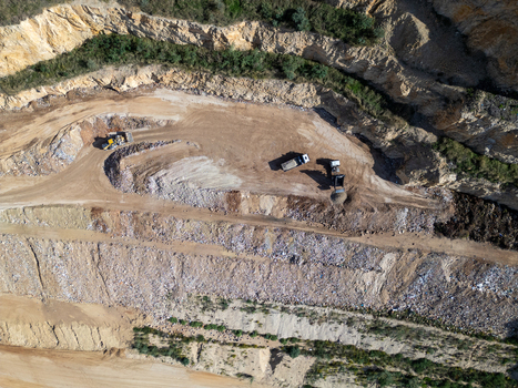 Aerial view of a quarry with heavy machinery including trucks and an excavator operating on terraced levels of earth and rock Teulada Valencian Community Spain.
