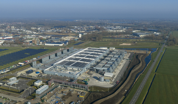 Aerial view of the Google data center with solar panels on the roof surrounding green fields and a canal under a clear blue sky in Winschoten Groningen Netherlands.