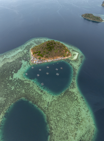 Aerial view of Pulau Kukusan with its small village and surrounding fish farms set in the clear turquoise waters of the coral reef in Komodo East Nusa Tenggara Indonesia. Aerial view of Pulau Kukusan with its small village and surrounding fish farms set in the clear turquoise waters of the coral reef in Komodo East Nusa Tenggara Indonesia.
