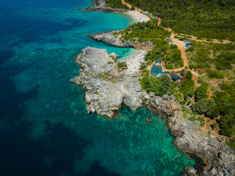 Aerial view of Aquarium Beach with turquoise waters rocky cliffs and lush green vegetation in Jala Vlore County Albania. Aerial view of Aquarium Beach with turquoise waters rocky cliffs and lush green vegetation in Jala Vlore County Albania.