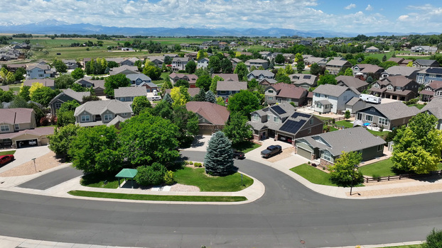 Aerial view of a suburban neighborhood with houses lush green trees solar panels on rooftops and paved streets under a bright blue sky in Fort Collins Colorado United States. Aerial view of a suburban neighborhood with houses lush green trees solar panels on rooftops and paved streets under a bright blue sky in Fort Collins Colorado United States.