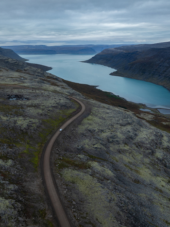 Aerial view of a winding road cuts through a rugged moss covered landscape leading towards the tranquil turquoise waters of the fjord Westfjords Iceland. Aerial view of a winding road cuts through a rugged moss covered landscape leading towards the tranquil turquoise waters of the fjord Westfjords Iceland.
