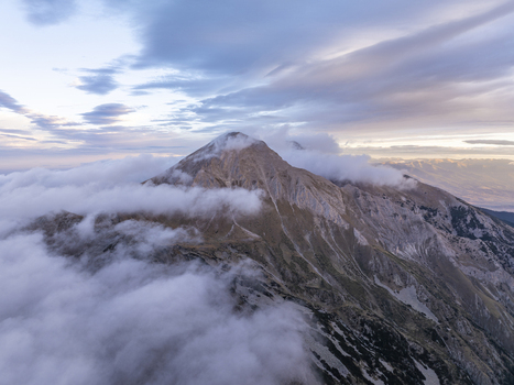 Aerial view of Pirin National Park featuring the rugged mountain peak rising above a sea of clouds under a soft sunset sky in Blagoevgrad Province Bulgaria. Aerial view of Pirin National Park featuring the rugged mountain peak rising above a sea of clouds under a soft sunset sky in Blagoevgrad Province Bulgaria.
