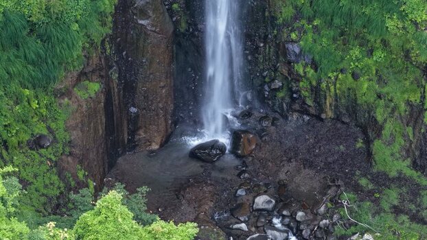 Aerial view of a waterfall cascading down a rocky cliff surrounded by lush green vegetation in Japan. Aerial view of a waterfall cascading down a rocky cliff surrounded by lush green vegetation in Japan.