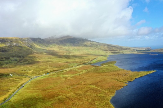 Aerial view of the dramatic landscape surrounding The Storr featuring a winding road along the shore of Loch Leathan under a cloudy sky in Portree Scotland United Kingdom.
