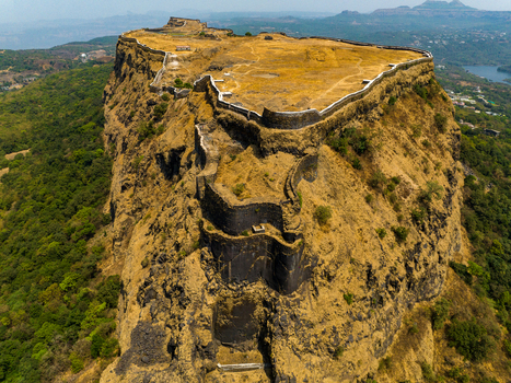 Aerial view of Korigad Fort with its historic stone fortifications and dry grassy plateau set against a backdrop of lush green hills and distant water in Peth Shahapur Maharashtra India. Aerial view of Korigad Fort with its historic stone fortifications and dry grassy plateau set against a backdrop of lush green hills and distant water in Peth Shahapur Maharashtra India.
