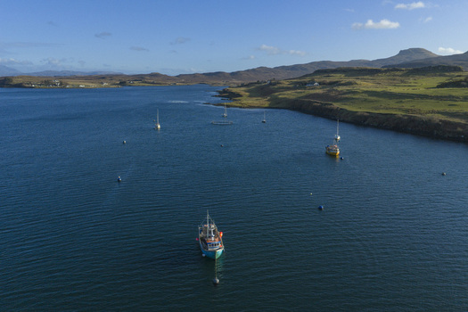 Aerial view of boats anchored in Loch Dunvegan with rolling green hills and a clear blue sky in Dunvegan Scotland United Kingdom. Aerial view of boats anchored in Loch Dunvegan with rolling green hills and a clear blue sky in Dunvegan Scotland United Kingdom.