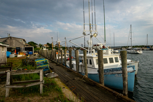 View of fishing boats docked at a wooden pier with lobster traps and fishing gear under a cloudy sky in Martha s Vineyard Edgartown Massachusetts United States.