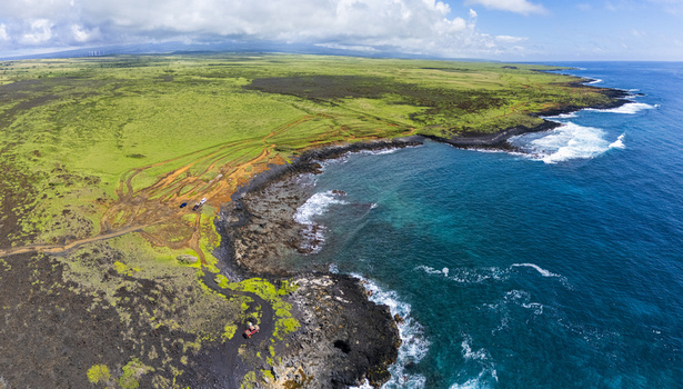 Aerial view of Kalae showing the rugged volcanic coastline turquoise ocean waters and green grassy plains under a cloudy sky Hawaii County Hawaii United States. Aerial view of Kalae showing the rugged volcanic coastline turquoise ocean waters and green grassy plains under a cloudy sky Hawaii County Hawaii United States.