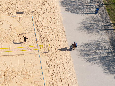 Vilnius Lithuania 20 April 2026 Aerial view of Chiune Sugihara Sakura Park featuring a sand volleyball court with a person playing and another person walking on the adjacent paved path under bright sunlight. Vilnius Lithuania 20 April 2026 Aerial view of Chiune Sugihara Sakura Park featuring a sand volleyball court with a person playing and another person walking on the adjacent paved path under bright sunlight.