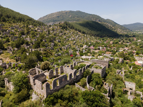 Aerial view of the historic stone ruins of the abandoned ghost village of Kayakoy surrounded by lush green hills and trees in Fethiye Mugla Turkey. Aerial view of the historic stone ruins of the abandoned ghost village of Kayakoy surrounded by lush green hills and trees in Fethiye Mugla Turkey.