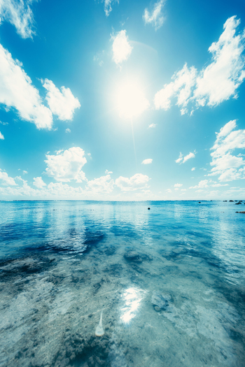 View of Rarotonga with crystal clear shallow water over a rocky seabed under a bright sun and blue sky in Cook Islands. View of Rarotonga with crystal clear shallow water over a rocky seabed under a bright sun and blue sky in Cook Islands.
