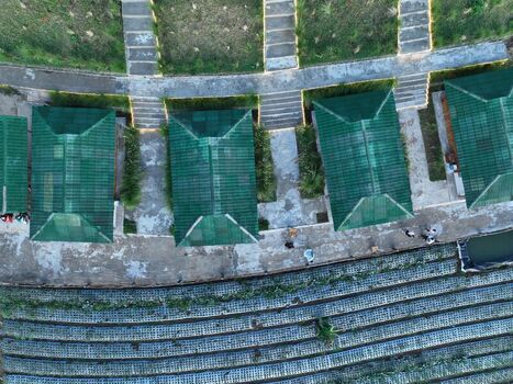 Aerial view of Linggar Jati featuring green roofed structures arranged along terraced agricultural fields in Kecamatan Kaliangkrik Jawa Tengah Indonesia. Aerial view of Linggar Jati featuring green roofed structures arranged along terraced agricultural fields in Kecamatan Kaliangkrik Jawa Tengah Indonesia.
