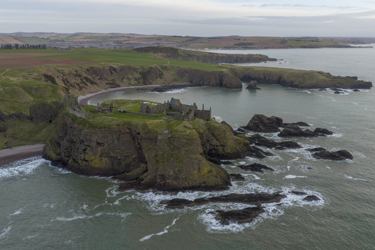 Aerial view of the medieval ruins of Dunnottar Castle perched on a dramatic rocky headland surrounded by the North Sea and green cliffs in Stonehaven Scotland United Kingdom. Aerial view of the medieval ruins of Dunnottar Castle perched on a dramatic rocky headland surrounded by the North Sea and green cliffs in Stonehaven Scotland United Kingdom.