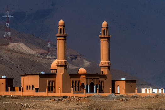 View of a mosque with two minarets and orange walls set against a rugged mountain landscape in Muscat Muscat Governorate Oman. View of a mosque with two minarets and orange walls set against a rugged mountain landscape in Muscat Muscat Governorate Oman.