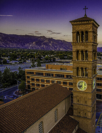 Aerial view of St. Andrew Catholic Church bell tower and its illuminated clock face with the San Gabriel Mountains at dusk in Pasadena California United States.