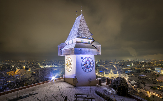 View of the iconic clock tower the Uhrturm standing majestically against the twilight sky casting a warm glow over the snow dusted city Graz Styria Austria. View of the iconic clock tower the Uhrturm standing majestically against the twilight sky casting a warm glow over the snow dusted city Graz Styria Austria.