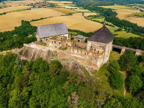 Aerial view of Tocnik Castle a historic medieval fortress with stone walls and wooden roofs situated on a forested hill surrounded by golden fields in Tocnik Stredocesky kraj Czechia. Aerial view of Tocnik Castle a historic medieval fortress with stone walls and wooden roofs situated on a forested hill surrounded by golden fields in Tocnik Stredocesky kraj Czechia.