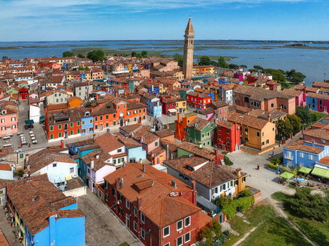 Aerial view of a vibrant tapestry of multicolored houses with terracotta roofs clustered tightly together punctuated by the soaring campanile of Burano Venice Veneto Italy. Aerial view of a vibrant tapestry of multicolored houses with terracotta roofs clustered tightly together punctuated by the soaring campanile of Burano Venice Veneto Italy.