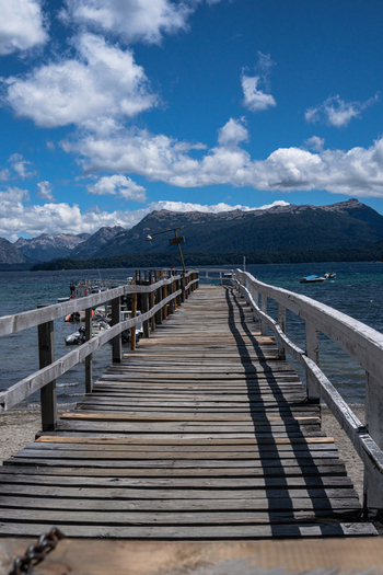 View of Bahia Brava pier extending into the lake with mountains in the background under a blue sky in Villa La Angostura Neuquen Province Argentina. View of Bahia Brava pier extending into the lake with mountains in the background under a blue sky in Villa La Angostura Neuquen Province Argentina.