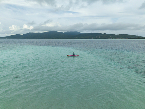 Aerial view of a lone kayaker on a pink kayak gliding across the turquoise waters near the distant island shores at Menjangan Kecil Island Karimunjawa Jawa Tengah Indonesia.