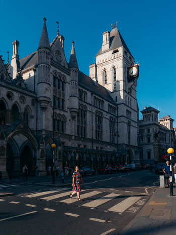 View of an ornate grey stone building with a clock tower under a blue sky contrasting with a person on a zebra crossing London England United Kingdom. View of an ornate grey stone building with a clock tower under a blue sky contrasting with a person on a zebra crossing London England United Kingdom.