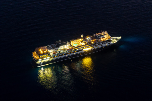Aerial view of an illuminated cruise ship sailing on the dark sea at night with bright deck lights and a swimming pool visible Eze Provence Alpes Cote d Azur France. Aerial view of an illuminated cruise ship sailing on the dark sea at night with bright deck lights and a swimming pool visible Eze Provence Alpes Cote d Azur France.