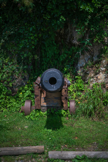 View of a historic iron cannon resting on a wooden carriage against an ivy covered stone wall in Charlestown Cornwall United Kingdom. View of a historic iron cannon resting on a wooden carriage against an ivy covered stone wall in Charlestown Cornwall United Kingdom.