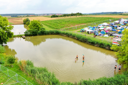 Herzogenaurach Germany 26 July 2025 Aerial view of the Open Beatz Festival campsite with people swimming in a pond and colorful tents pitched on the grass.