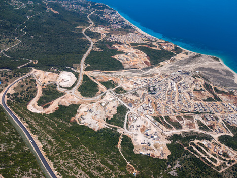 Aerial view of a winding road passing through green hills and coastal construction sites near the turquoise sea in Palase Vlore County Albania.