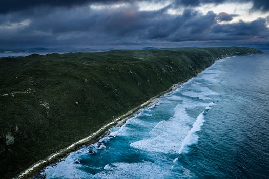 Aerial view of the rugged Sandpatch coastline with dramatic dark clouds over the ocean crashing waves and lush green cliffs in Albany Western Australia Australia. Aerial view of the rugged Sandpatch coastline with dramatic dark clouds over the ocean crashing waves and lush green cliffs in Albany Western Australia Australia.