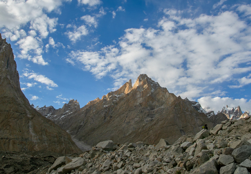 View of the rugged granite spires of the Trango Towers under a bright blue sky with scattered clouds and a rocky glacial moraine in the foreground in Pakistan. View of the rugged granite spires of the Trango Towers under a bright blue sky with scattered clouds and a rocky glacial moraine in the foreground in Pakistan.
