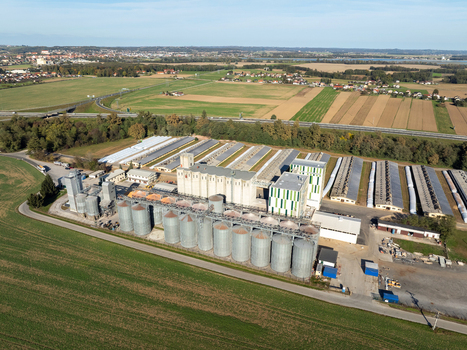 Aerial view of a large industrial grain storage facility with silver silos and warehouses surrounded by agricultural fields and a highway in Slovenia. Aerial view of a large industrial grain storage facility with silver silos and warehouses surrounded by agricultural fields and a highway in Slovenia.