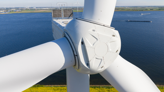 Aerial view of a white wind turbine nacelle and rotor hub overlooking a blue waterway with a passing barge and distant turbines in Ooltgensplaat Zuid Holland Netherlands. Aerial view of a white wind turbine nacelle and rotor hub overlooking a blue waterway with a passing barge and distant turbines in Ooltgensplaat Zuid Holland Netherlands.