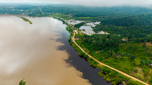 Aerial view of the river confluence near Itu featuring contrasting water currents lush tropical vegetation and a dirt road along the riverbank in Itu Akwa Ibom Nigeria. Aerial view of the river confluence near Itu featuring contrasting water currents lush tropical vegetation and a dirt road along the riverbank in Itu Akwa Ibom Nigeria.
