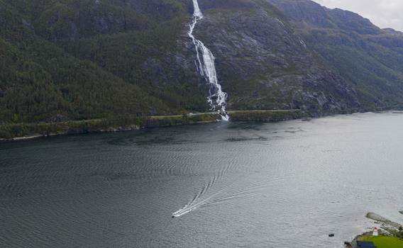 Aerial view of Langfossen waterfall cascading down a steep rocky mountain into the fjord with a boat cruising on the water Fjaera Vestland Norway. Aerial view of Langfossen waterfall cascading down a steep rocky mountain into the fjord with a boat cruising on the water Fjaera Vestland Norway.