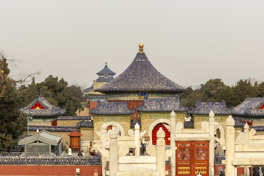 View of the Temple of Heaven complex featuring traditional blue tiled roofs red gates and white marble structures with people walking around Beijing Beijing China. View of the Temple of Heaven complex featuring traditional blue tiled roofs red gates and white marble structures with people walking around Beijing Beijing China.