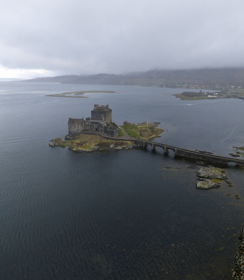 Aerial view of Eilean Donan Castle on its tidal island with the stone bridge over the calm waters of Loch Duich under a misty sky in Dornie Scotland United Kingdom.